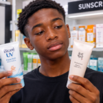 Male Nigerian teenager comparing Biore and Beauty of Joseon sunscreens for his skincare routine.