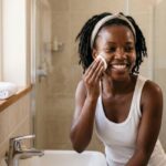 Dark-skinned African woman applying exfoliating peel pads to her face for smoother, brighter-looking skin during a skincare routine.