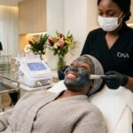 African woman wearing a charcoal face mask during a professional skincare treatment in a modern face spa studio.