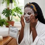  African woman applying a hydrating sheet mask during a skincare routine for dry and dehydrated skin in Nigeria.