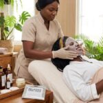 African woman receiving a sheet mask facial treatment from a spa attendant during a relaxing skincare session in a Nigerian spa.