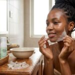 African woman gently removing a peel-off face mask during her skincare routine for clear and glowing skin.