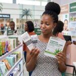 African woman comparing and purchasing peel-off masks and sheet masks at a cosmetic store in a Nigerian shopping mall.